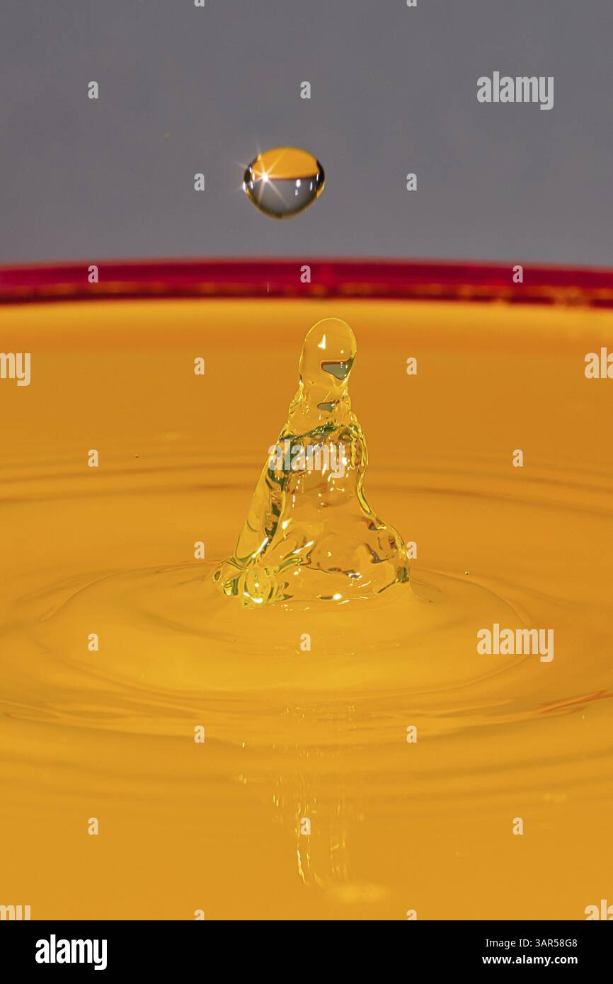 Une goutte d’or frappe une surface orange et forme des sculptures rayonnantes, des gouttelettes d’eau, des collisions, des photographies à grande vitesse, des concepts Banque D'Images