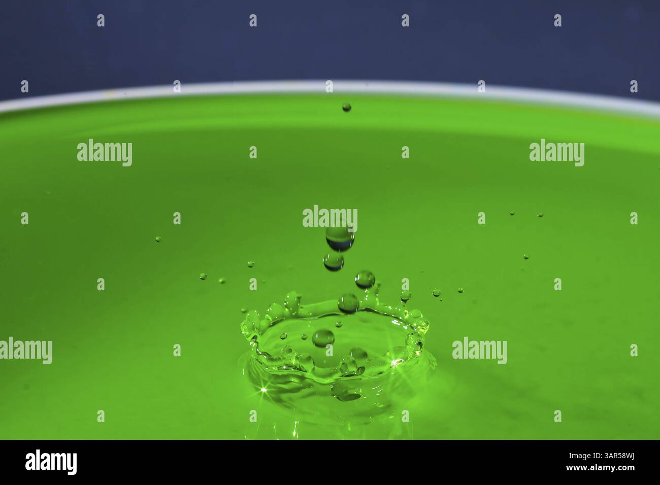 Une goutte verte crée une couronne d'éclaboussures sur la surface du liquide, des gouttelettes d'eau, collision, photographie à grande vitesse, concept Banque D'Images