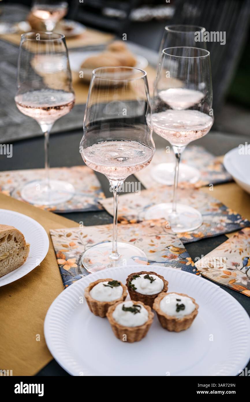 Trois verres de vin rosé mousseux entourés d'assiettes de pain et de tartes salées sur une table à manger de jardin. Repas attentifs, détox numérique, connexion Banque D'Images