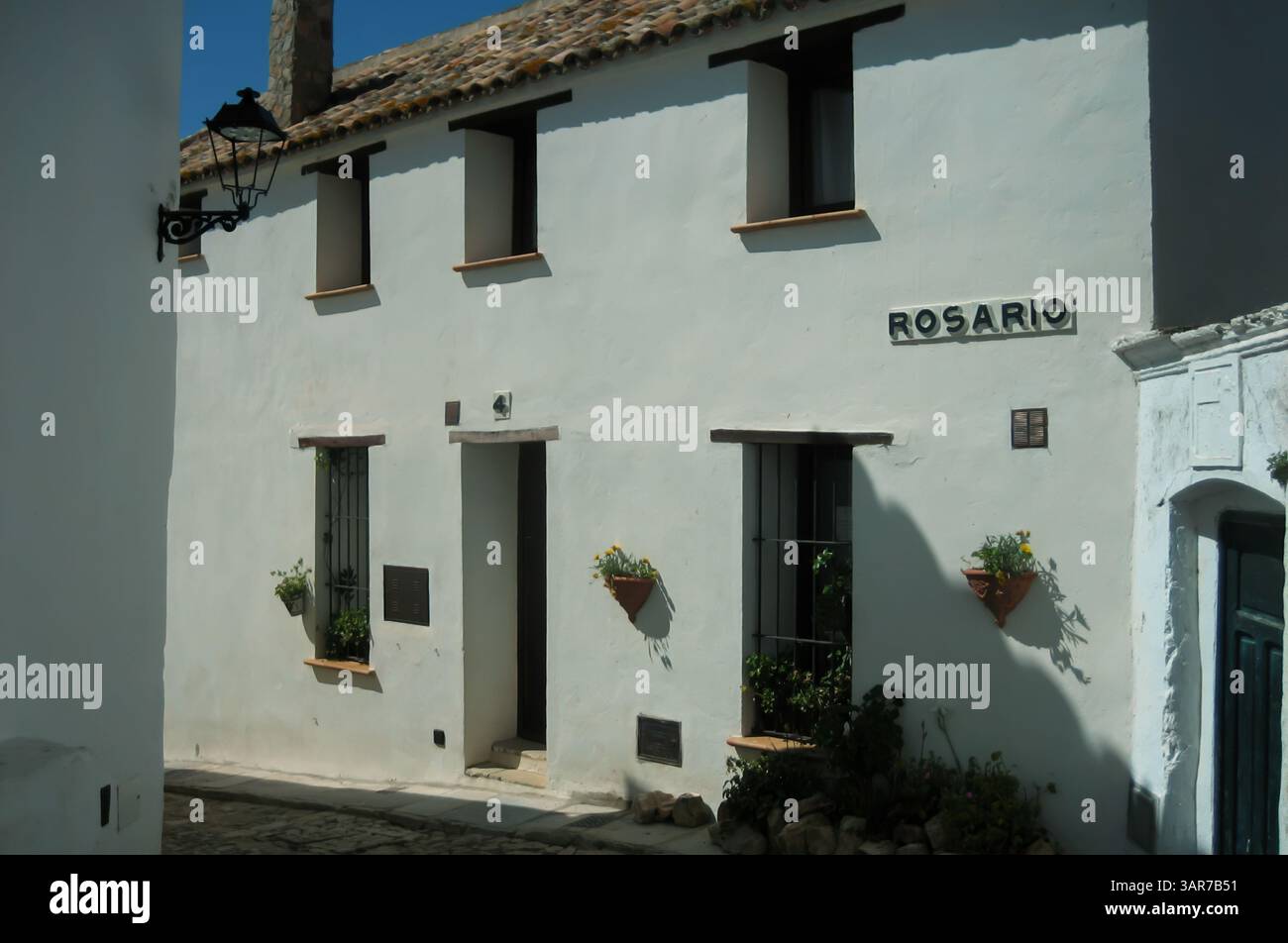 Bâtiment traditionnel blanchi à la chaux avec panneau de rue rosario et pots de fleurs dans un village espagnol pittoresque Banque D'Images