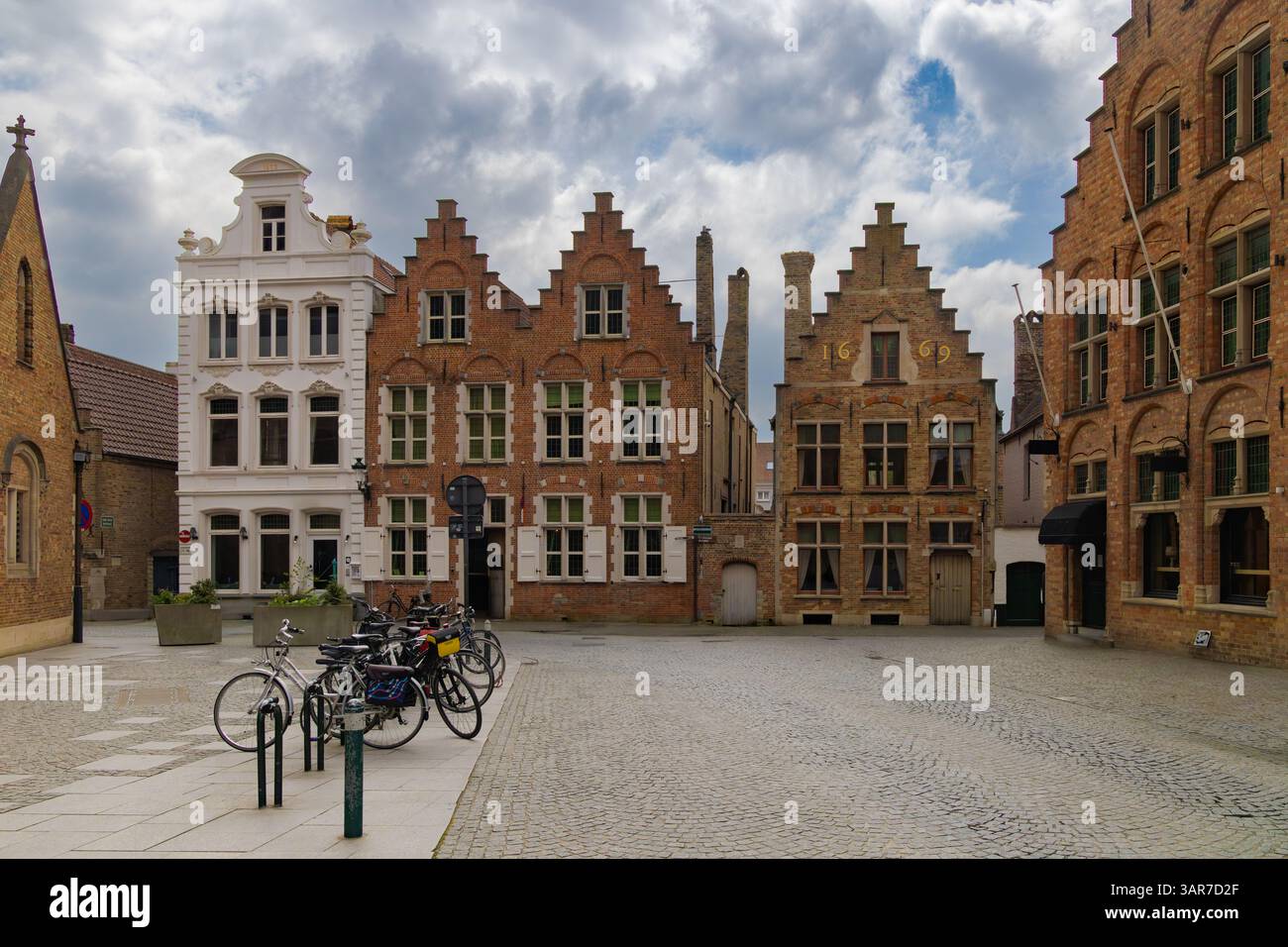 Les maisons traditionnelles à pignon en escalier bordent une place pavée dans la ville historique de Bruges, en Belgique, avec des vélos garés sous un ciel nuageux. Banque D'Images