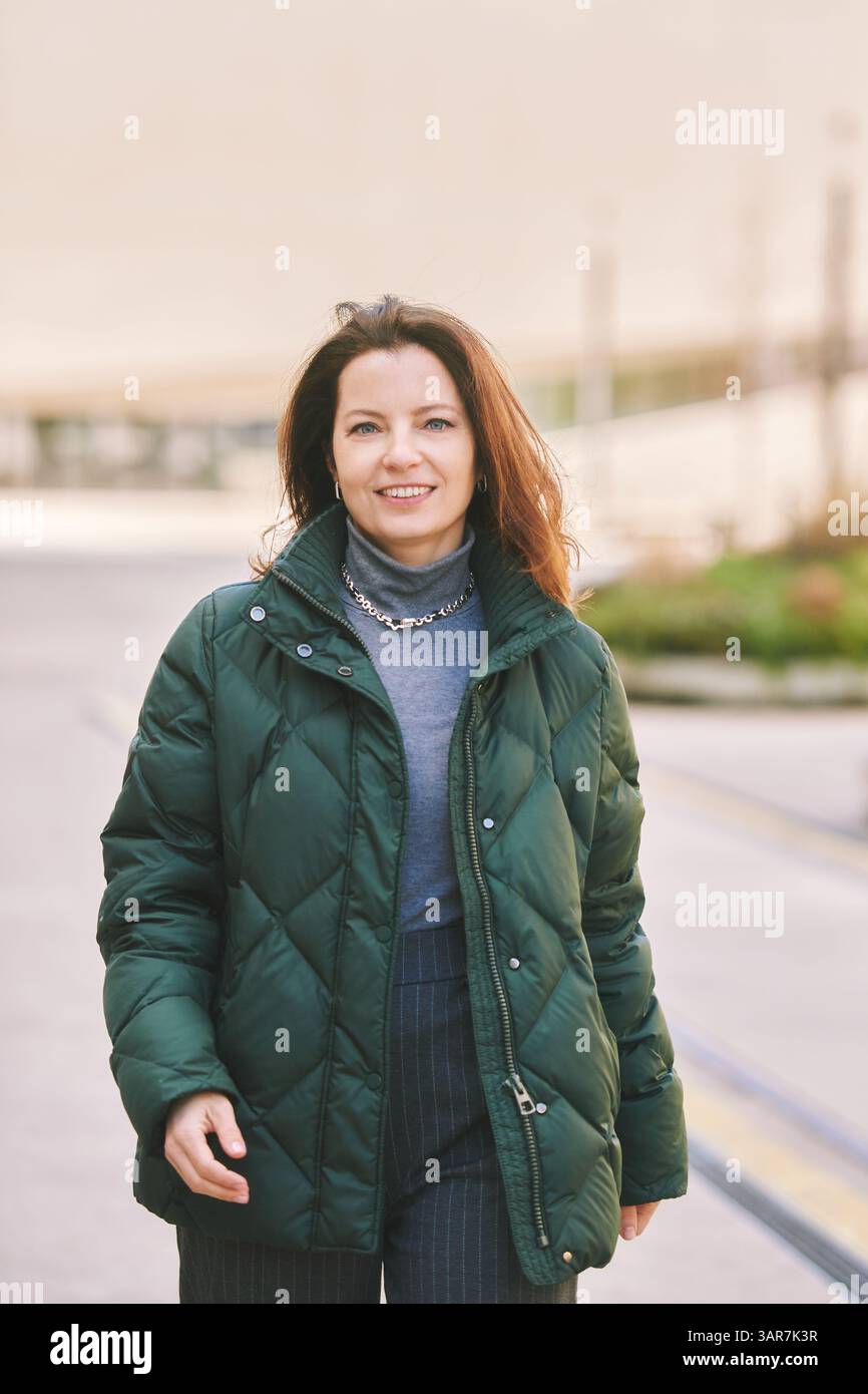 Portrait extérieur de la femme heureuse d'âge moyen marchant dans la rue, portant une veste verte chaude Banque D'Images