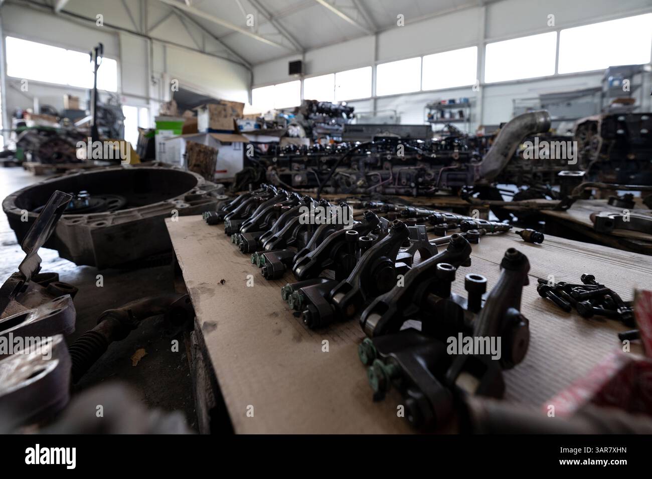 Divers composants de moteur démontés sont soigneusement disposés sur un établi dans un atelier de réparation spacieux ou un entrepôt rempli d'autres pièces de moteur et eq Banque D'Images