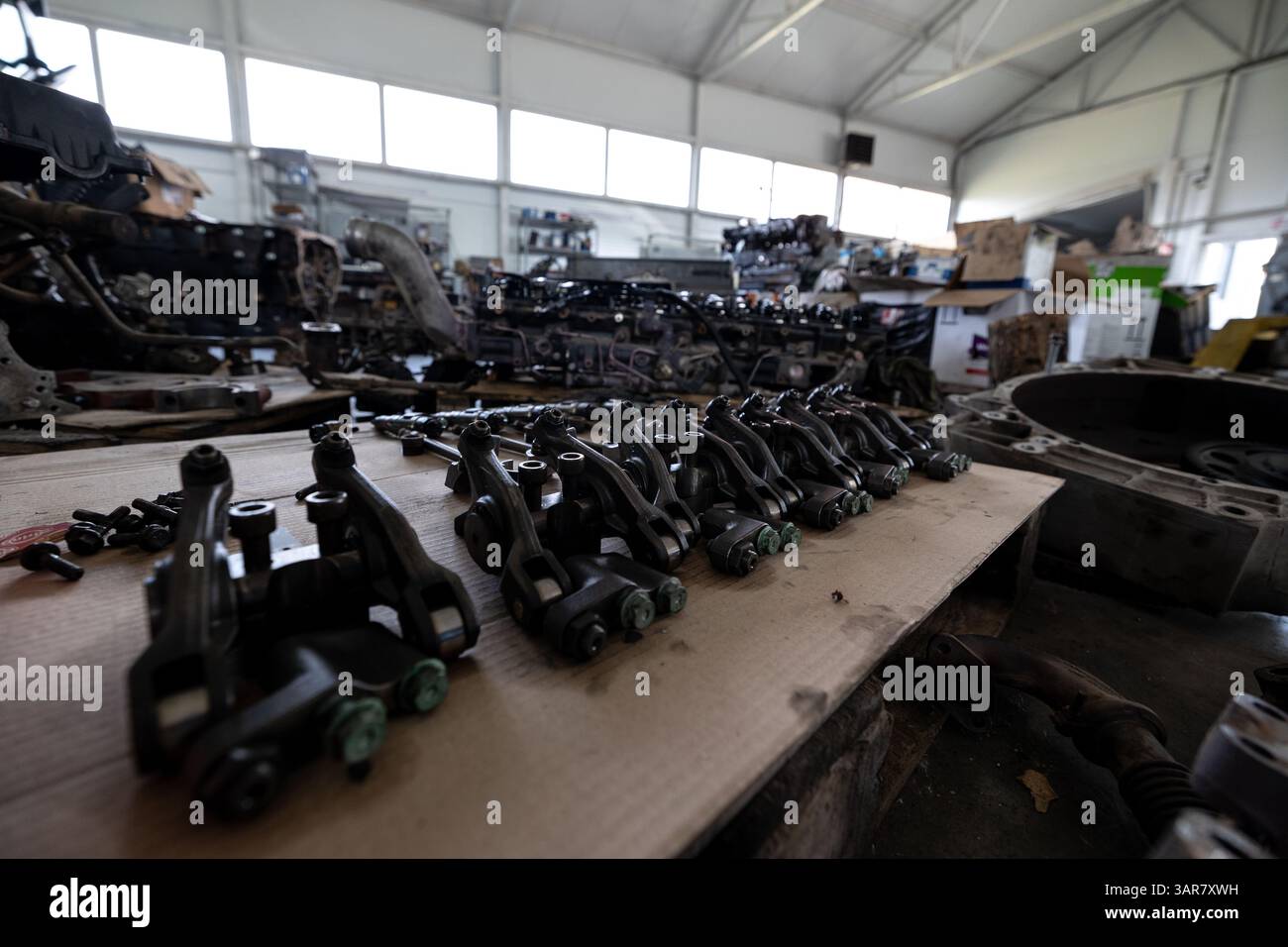 Divers composants de moteur démontés sont soigneusement disposés sur un établi dans un atelier de réparation spacieux ou un entrepôt rempli d'autres pièces de moteur et eq Banque D'Images