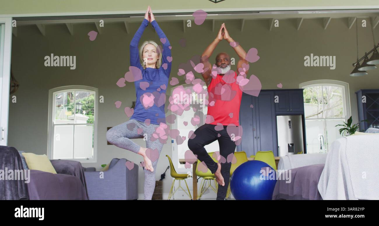 Image d'icônes de coeur sur couple senior diversifié pratiquant le yoga à la maison Banque D'Images
