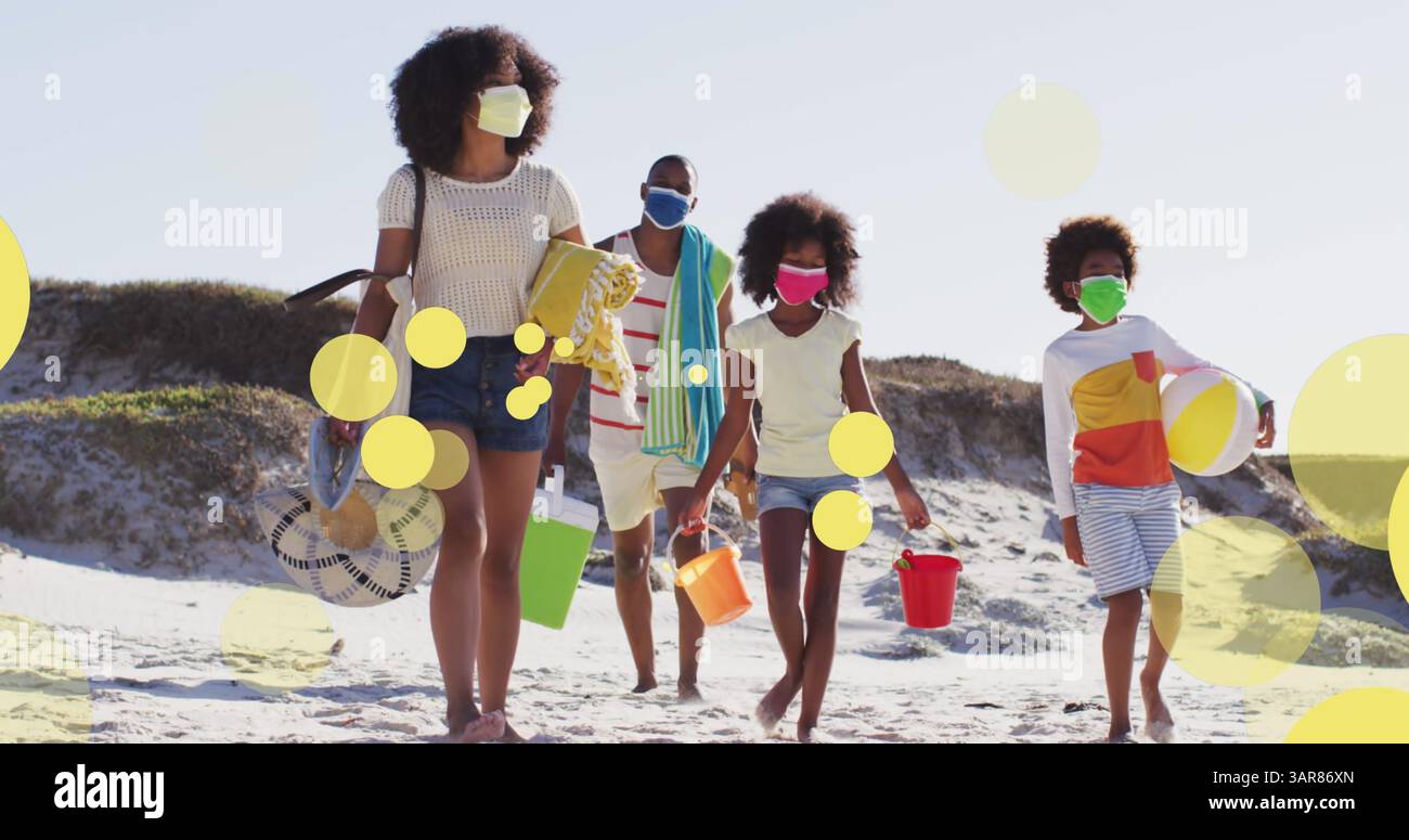 Image d'une famille afro-américaine avec des masques de visage marchant à la plage au-dessus de taches lumineuses Banque D'Images