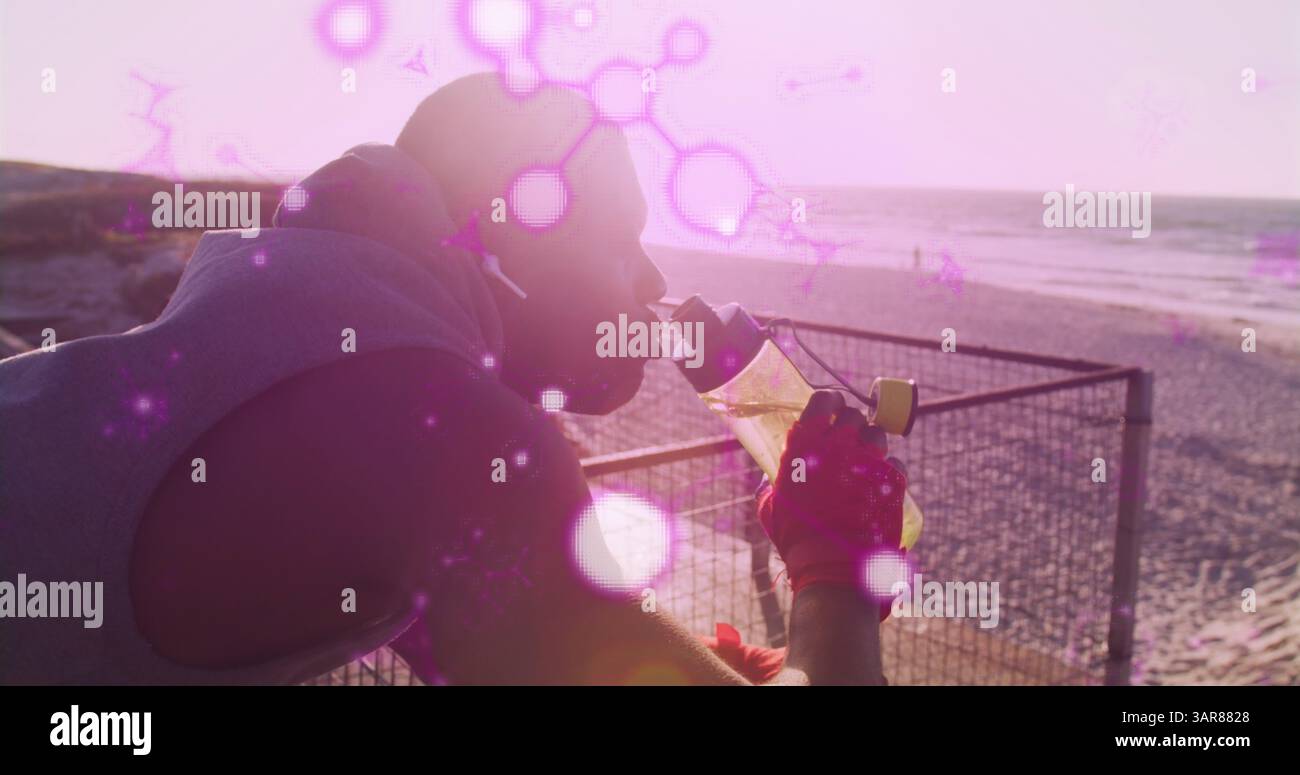 Structures moléculaires brillantes flottant contre l'homme afro-américain apte à boire de l'eau près de la plage Banque D'Images