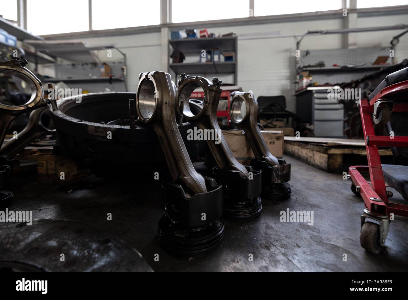 Les pistons avec bielles sont disposés sur le plancher d'un atelier de réparation ou d'un entrepôt, entourés par d'autres composants et outils de moteur. Banque D'Images