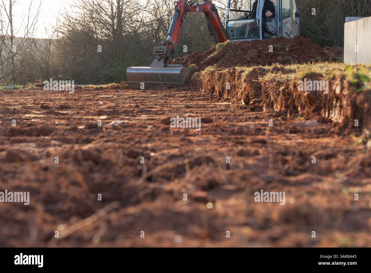 La pelle, équipée d'un godet, râteau un sol argileux mélangé à des pierres. La machinerie lourde travaille avec diligence sur le chantier de construction Banque D'Images