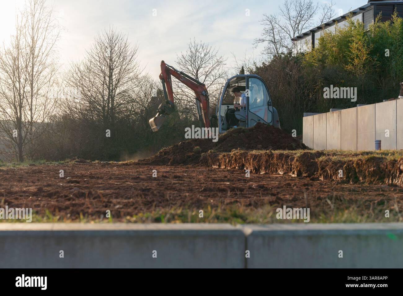 Excavatrice avec godet déblayant l'argile et le sol rocheux sur un chantier de construction. Machinerie lourde préparant le terrain pour les travaux de construction dans une zone résidentielle Banque D'Images