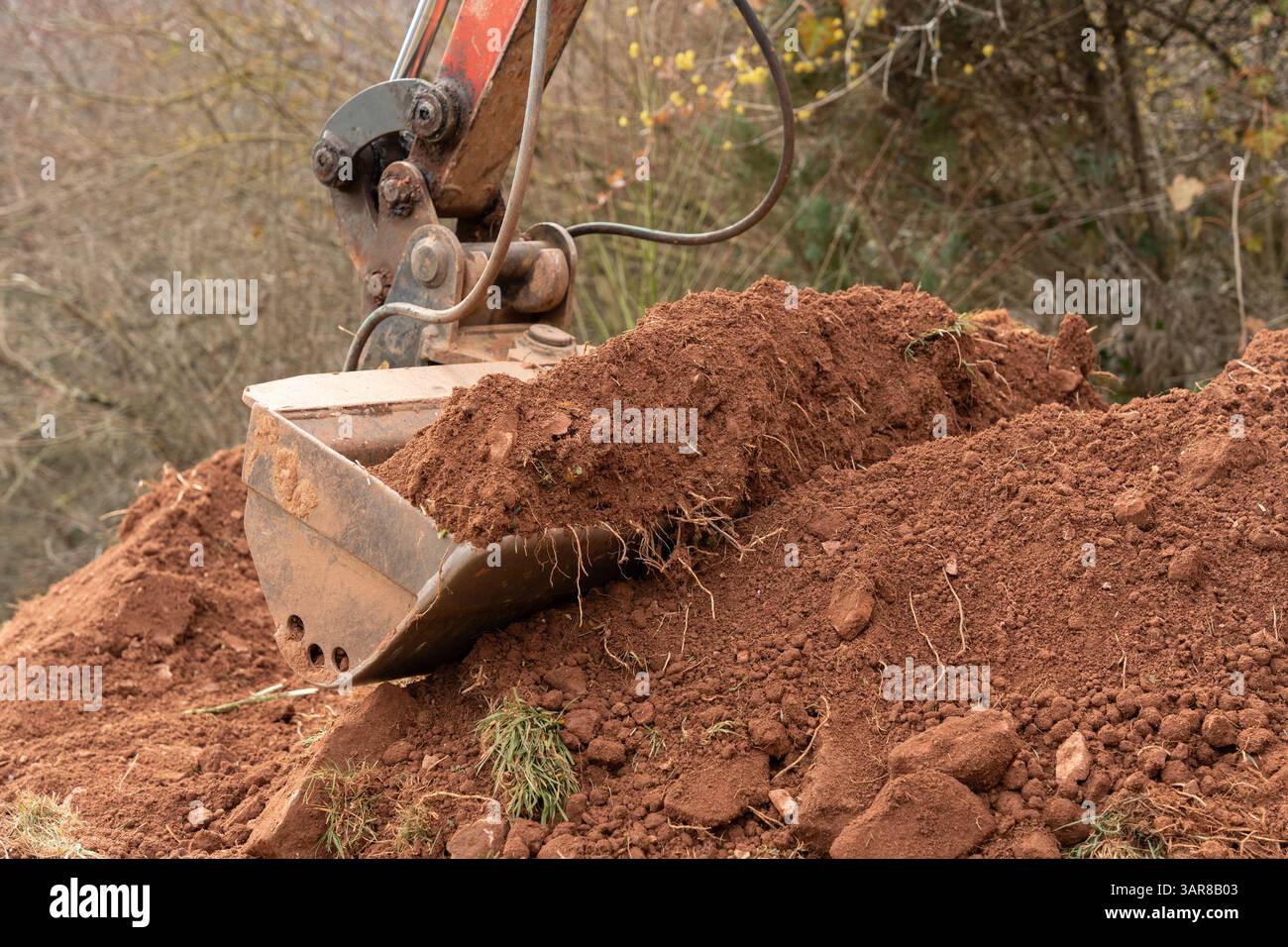 Le godet excavateur rempli de terre argileuse et de pierres, creusant dans la terre. La machinerie lourde fonctionne sur un chantier de construction, préparant le Banque D'Images