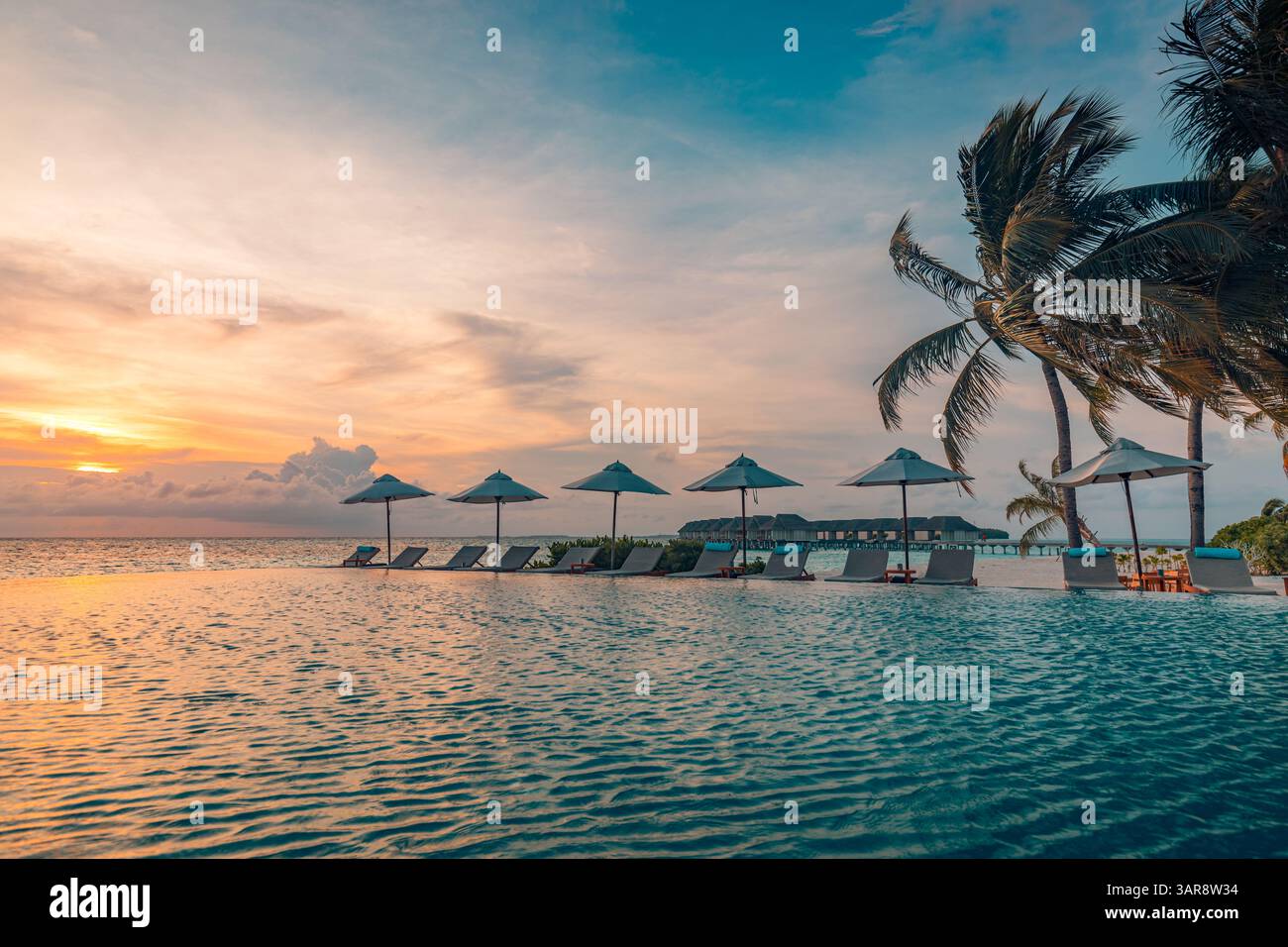 Coucher de soleil piscine à débordement chaises longues parasol feuilles de palmier. Vacances d'été luxueuses vacances tropicales tourisme de villégiature, nuages colorés de ciel de mer. Tourisme époustouflant Banque D'Images