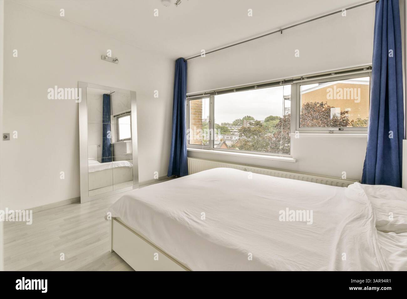 Une chambre lumineuse et contemporaine avec de grandes fenêtres, des rideaux élégants et un design minimaliste qui rehausse l'atmosphère spacieuse de la pièce. Banque D'Images