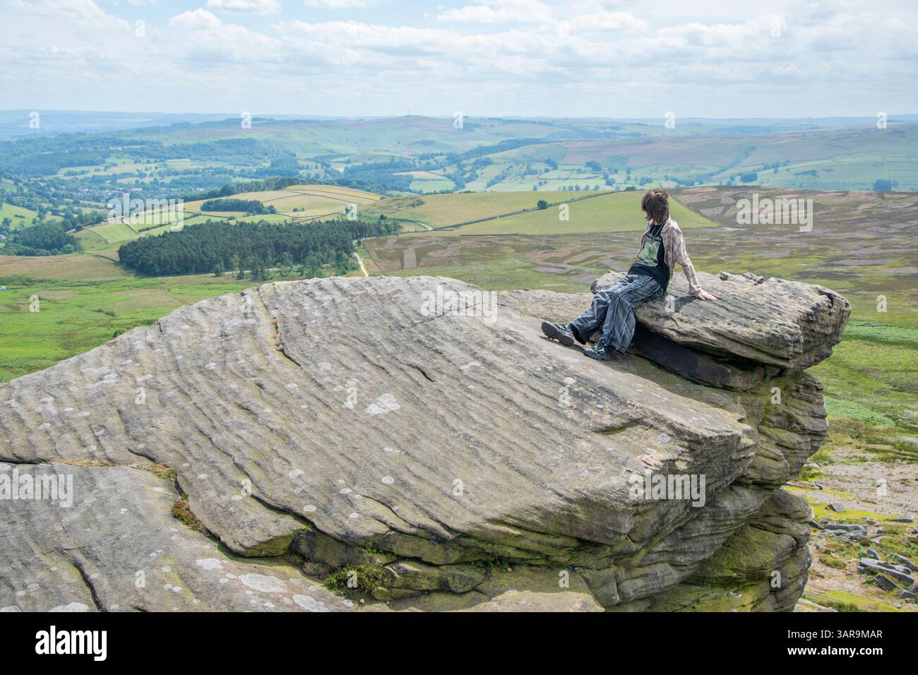 Derbyshire, Royaume-Uni – 5 juillet 2024 : Teenage Girl s'est assise sur un rocher au sommet d'une falaise en profitant de la vue sur le Peak District depuis Stanage Edge Banque D'Images