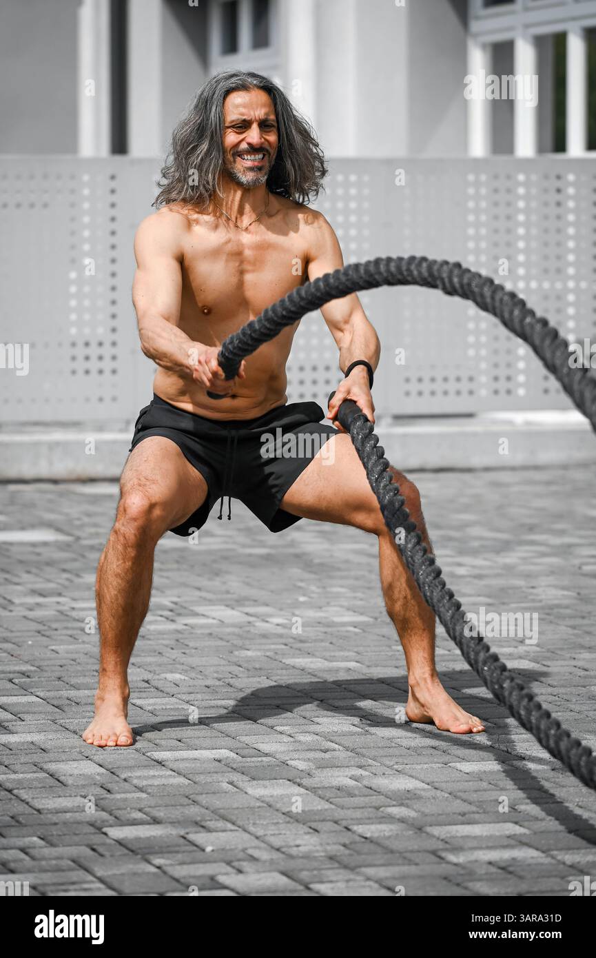 Sportif exerçant avec des cordes de combat pendant l'entraînement de fitness en extérieur Banque D'Images