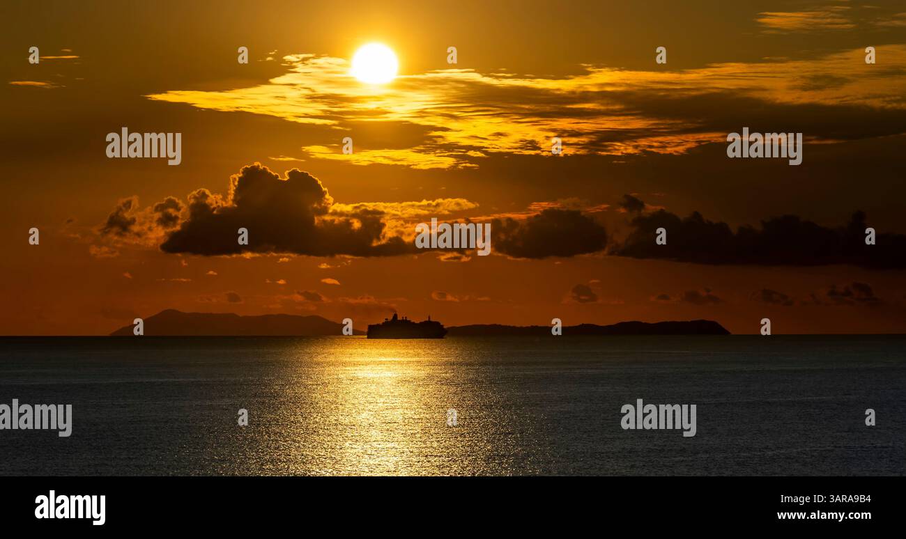 Un coucher de soleil serein sur l'océan, avec un grand navire silhouette contre l'horizon brillant. Le ciel est rempli de nuages illuminés par le chaud golde Banque D'Images