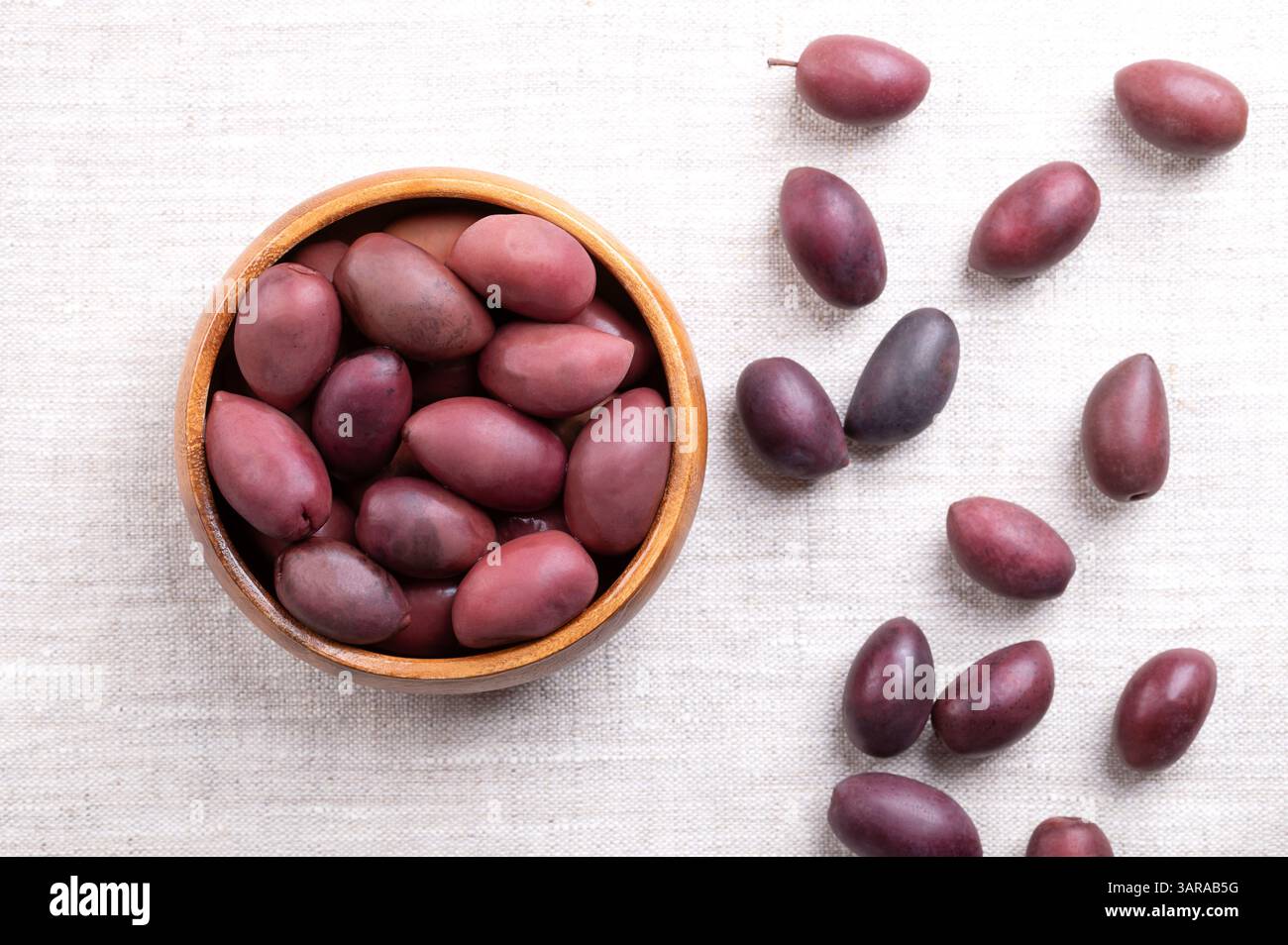 Olives Kalamata avec fosse, dans un bol en bois sur lin. Grandes olives violettes cueillies à la main, à la texture lisse et charnue, nommées d'après la ville grecque Kalamata. Banque D'Images