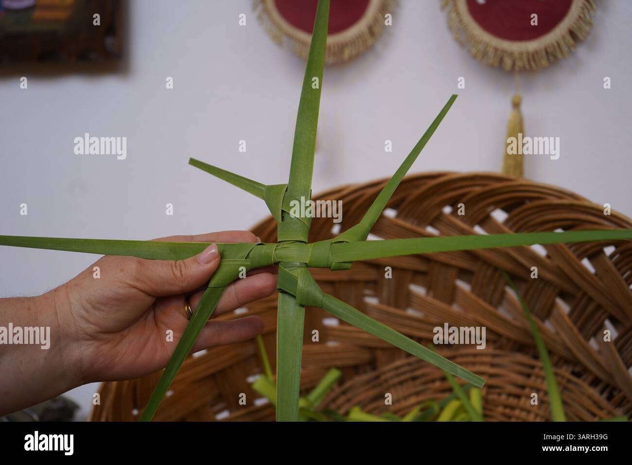Coutume de Pâques : la main de la femme tient une croix faite à la main qui a été faite à partir de feuille de palmier - plus de croix sont dans un panier tissé qui vont être partagés Banque D'Images