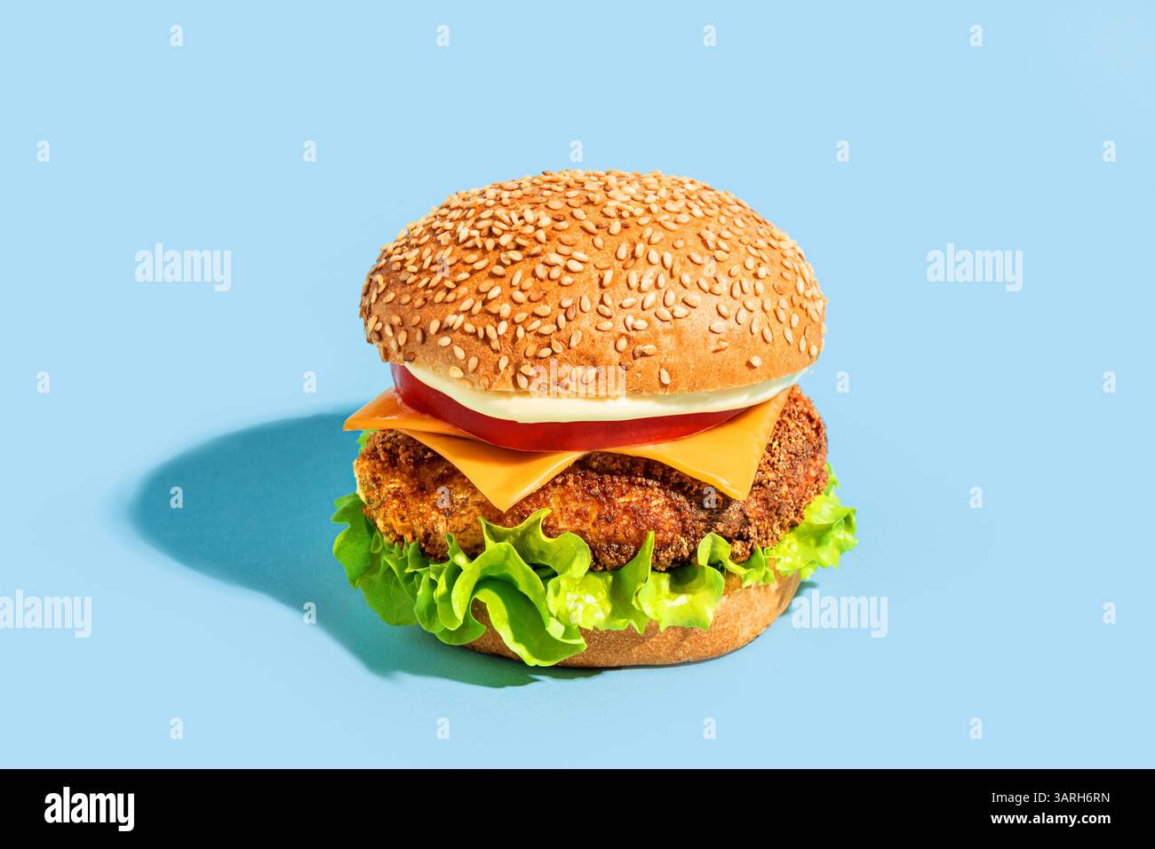 Burger de poulet, cheeseburger sur fond bleu vif, design créatif. Cheeseburger ultime avec fromage cheddar, laitue, tomate et pain frais. Bur Banque D'Images
