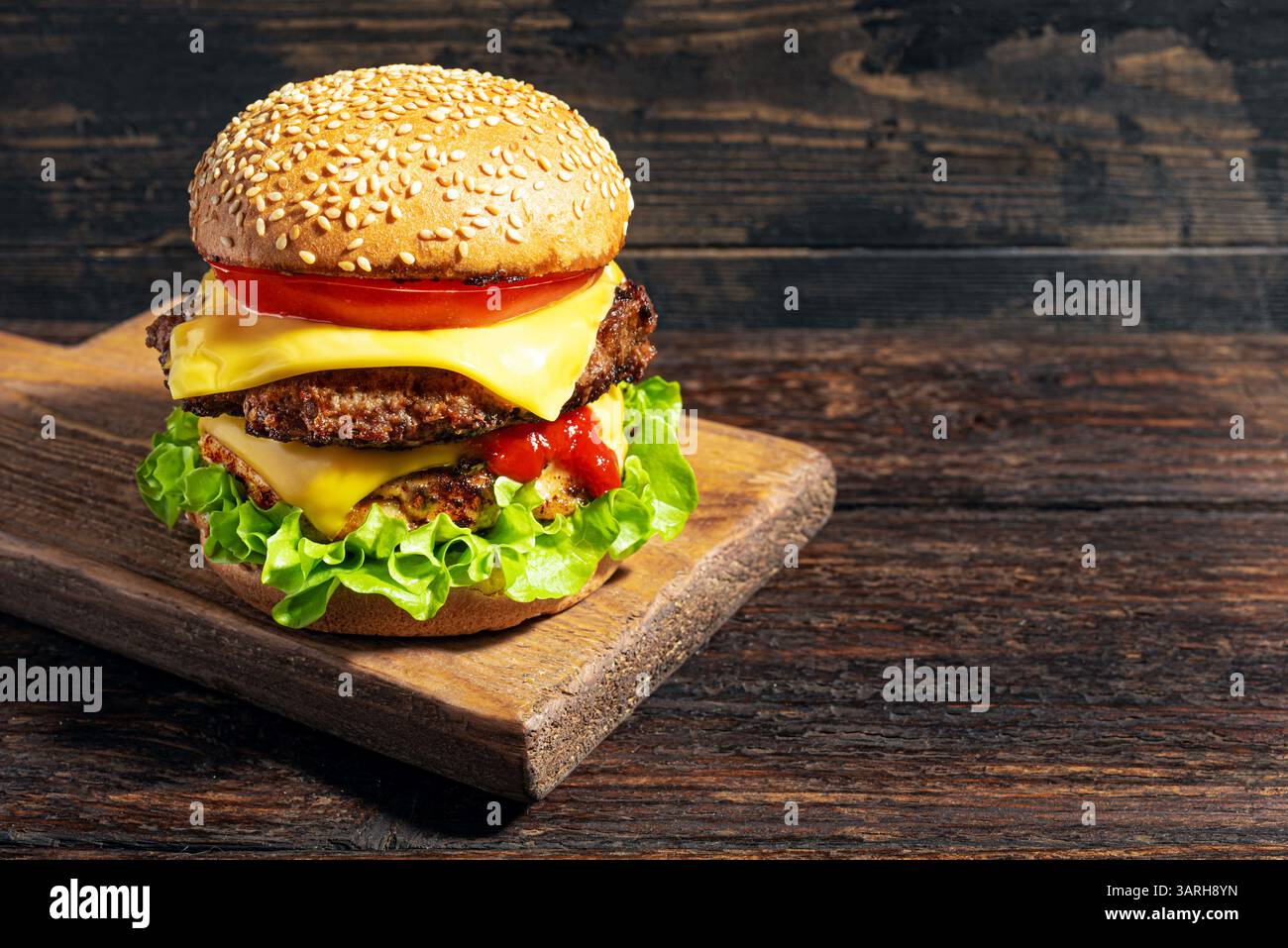 Double cheeseburger avec laitue, tomate, ketchup et fromage américain fondu sur fond de bois foncé, espace de copie. Big burger avec de la viande supplémentaire. Hambur Banque D'Images