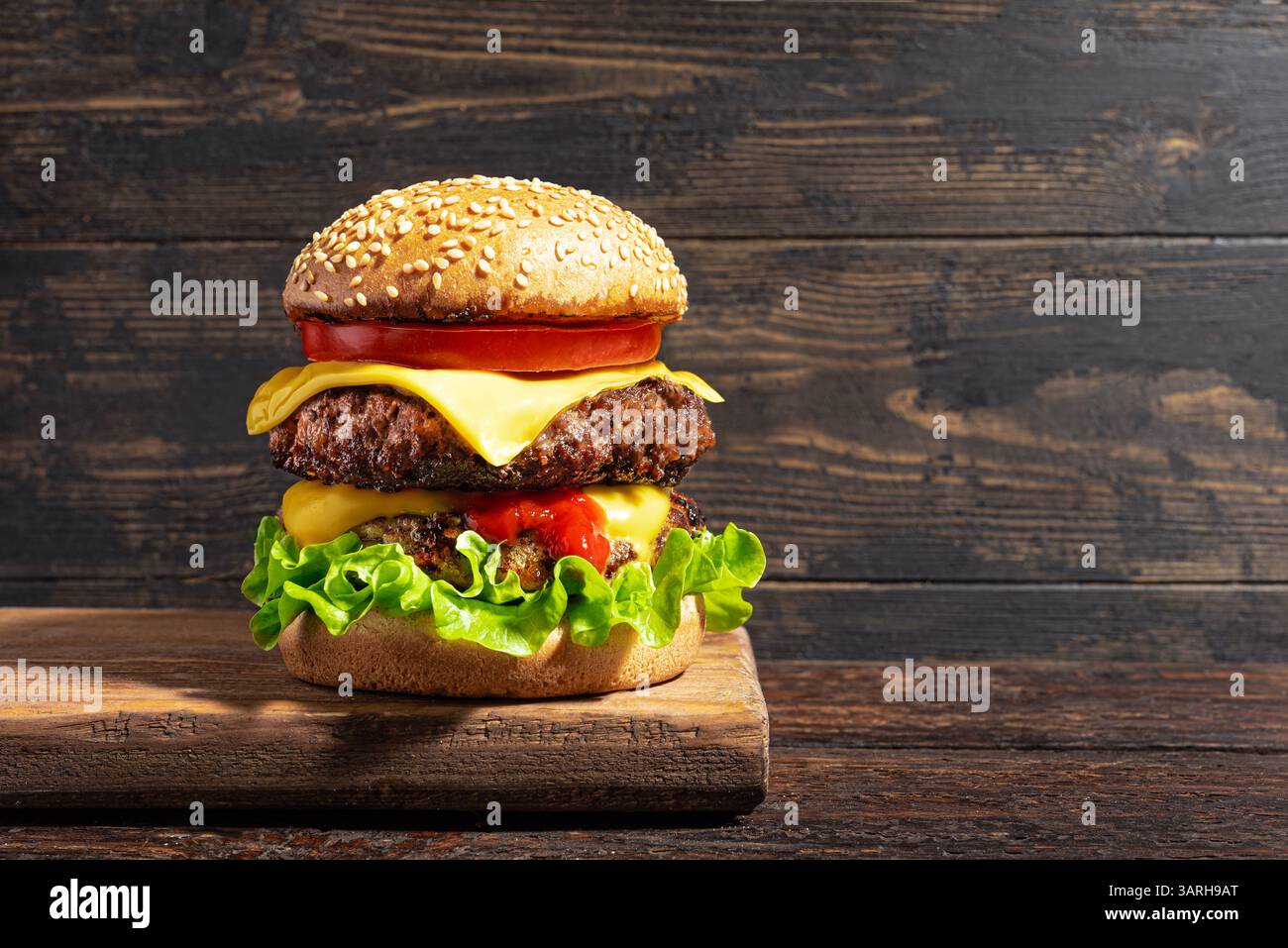 Double burger de bœuf, cheeseburger avec des légumes et du fromage américain fondu sur fond de bois rustique, espace de copie. Grand hamburger de viande supplémentaire ultime. H Banque D'Images