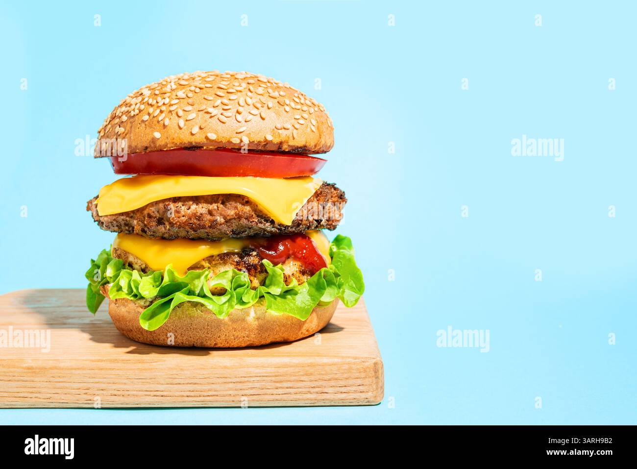 Double cheeseburger avec laitue, tomate, ketchup et fromage américain fondu sur fond bleu, espace de copie. Big burger avec de la viande supplémentaire. Hamburger par Banque D'Images