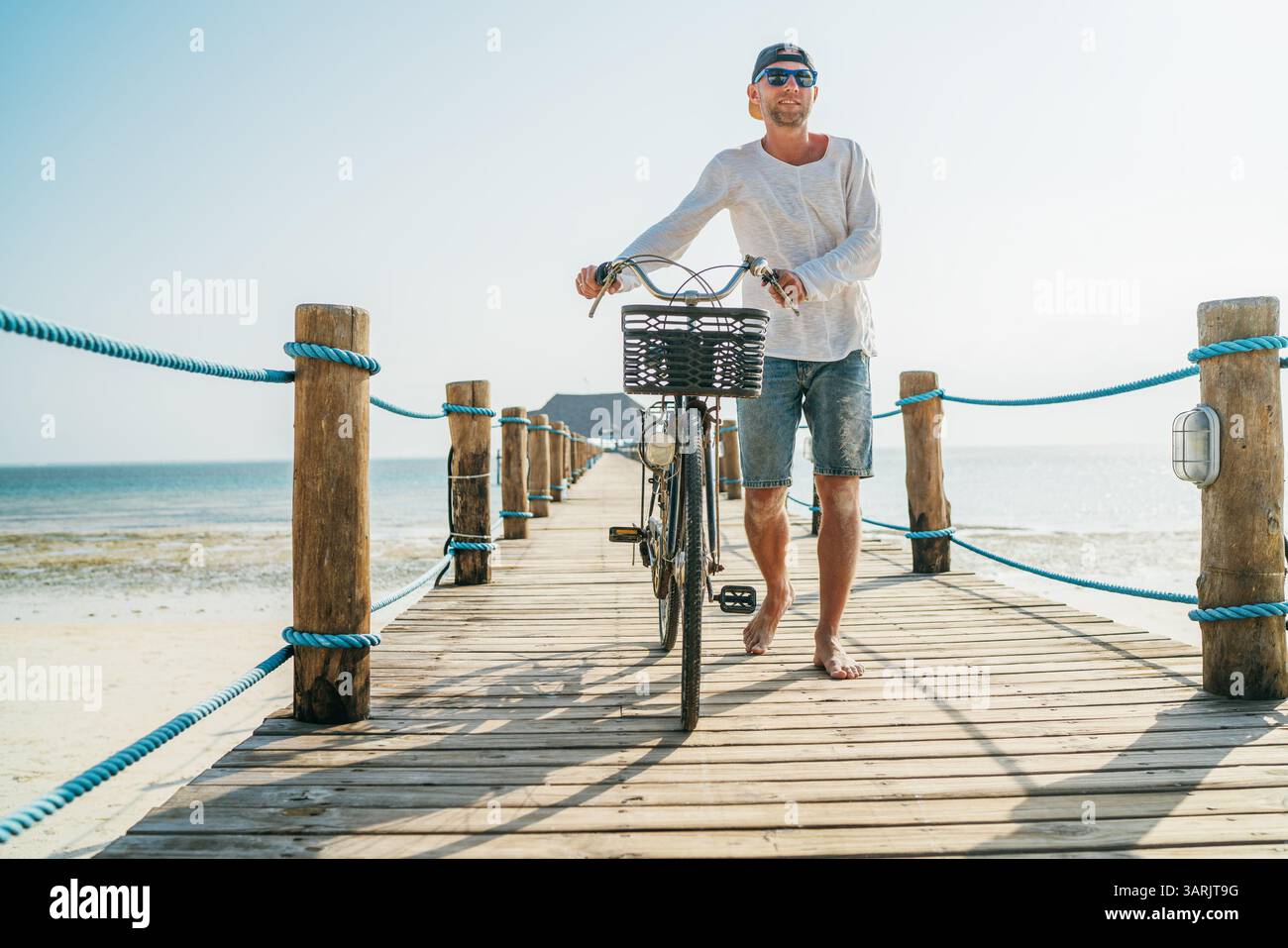 Portrait d'homme vêtu de vêtements d'été légers, lunettes de soleil avec vieux vélo sur la jetée en bois sur la plage de sable de Zanzibar. Vacances imprudentes en t Banque D'Images