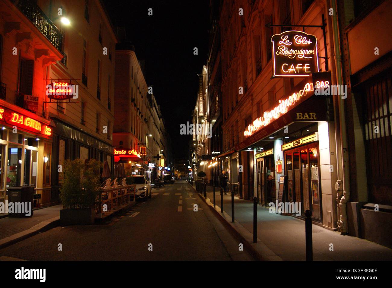 Une charmante rue parisienne illuminée par la lueur chaude des enseignes au néon et des lumières la nuit, mettant en valeur l'ambiance animée de la ville après la tombée de la nuit. Banque D'Images