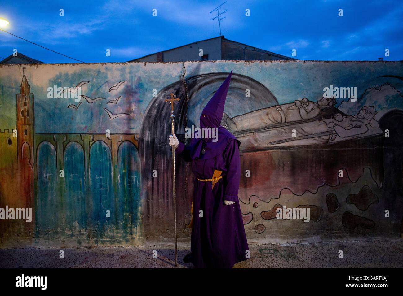 Sahagun, Espagne. 17 avril 2025. Un pénitent de la Fraternité de notre Père Jésus de Nazareth et du patronage de Saint Joseph se tient contre un mur peint avec des images de la tombe du roi Léonien Alphonse VI, lors de la procession du jeudi Saint, qui a traversé les rues principales de Sahagun. Crédit : SOPA images Limited/Alamy Live News Banque D'Images