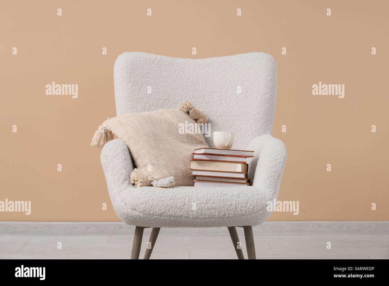 Fauteuil blanc avec pile de livres et thé près du mur beige Banque D'Images