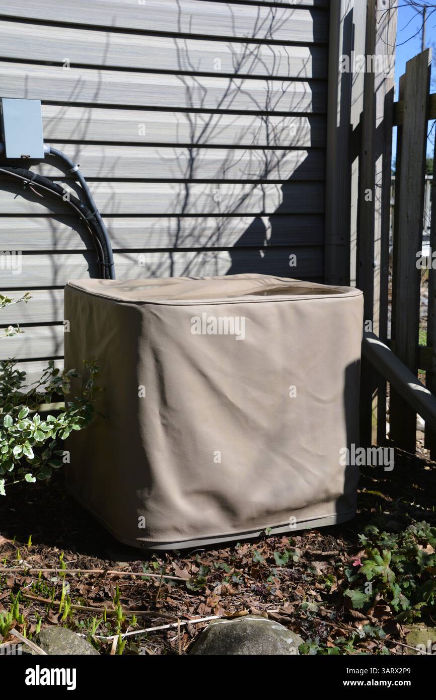 Une unité de condenseur de climatisation centrale extérieure est recouverte d'une couverture de stockage beige protectrice à l'extérieur d'une maison résidentielle. Banque D'Images