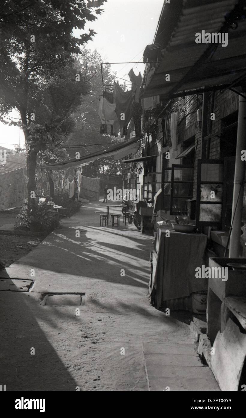 La lumière du soleil jette de longues ombres sur une rue calme dans un quartier vintage rempli d'art textile et de moments de la vie quotidienne : blanchisserie suspendue et allée ensoleillée dans une cour résidentielle du lac de l'Ouest Hangzhou, début des années 2000, Hangzhou, Zhejiang, Shandong Banque D'Images
