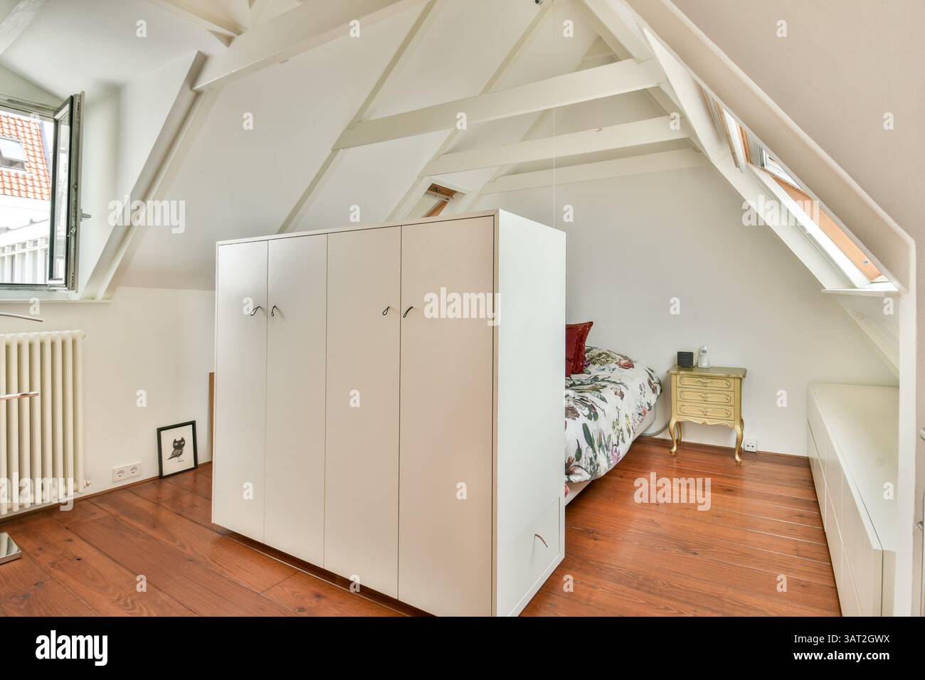 Une chambre minimaliste chaleureuse et accueillante avec armoires blanches, parquet et lumière naturelle qui traverse la fenêtre, créant une atmosphère sereine. Banque D'Images