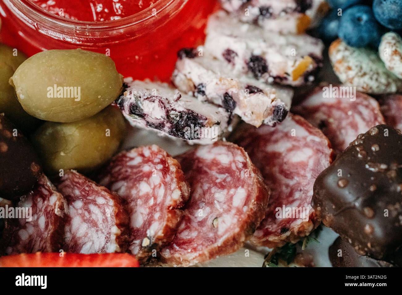 Gros plan de tranches de salami, fromage, olives et confiture rouge. Banque D'Images
