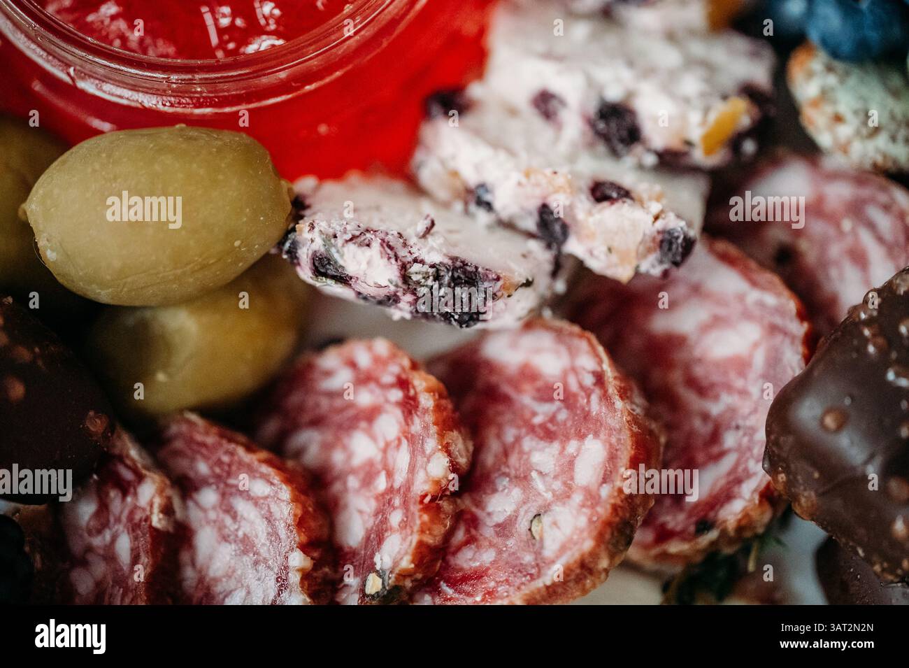 Gros plan de tranches de salami, fromage, olives et confiture rouge. Banque D'Images