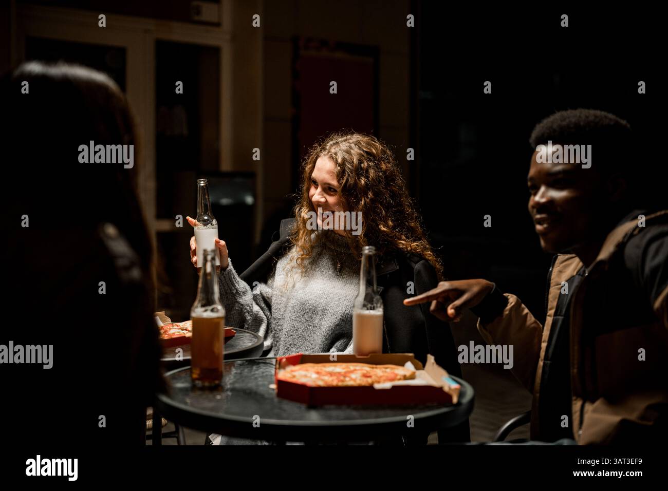 Amis appréciant pizza et boissons la nuit dans un lieu de rencontre local confortable Banque D'Images