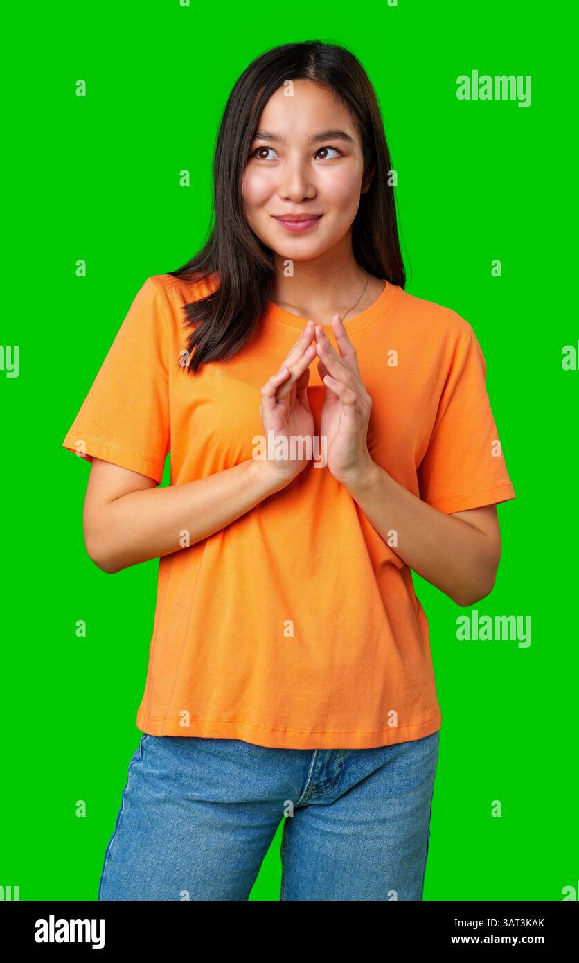 Jeune femme en t-shirt orange souriant et posant de manière ludique sur fond vert solide Banque D'Images