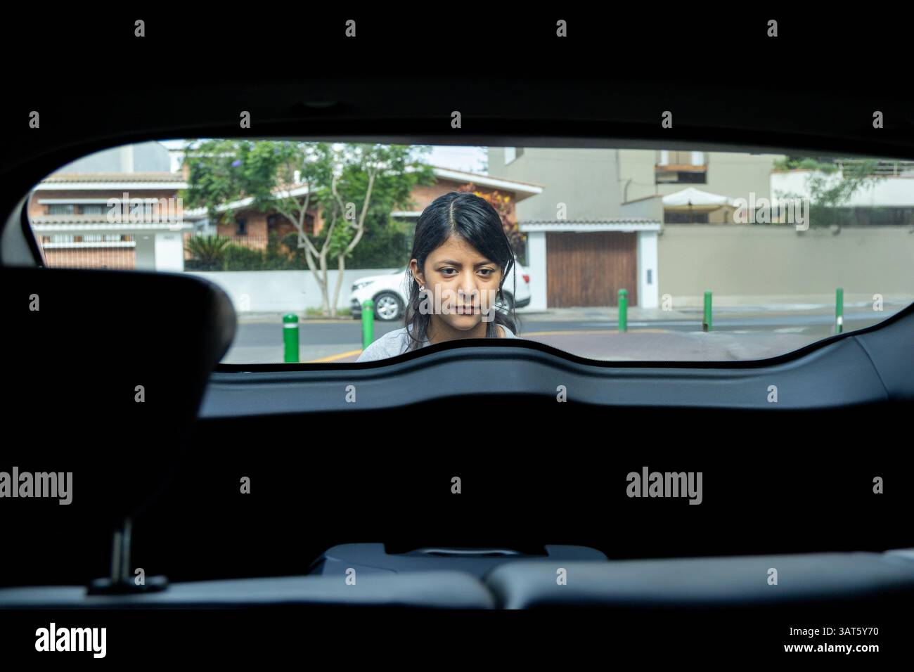 Un adolescent regarde par la vitre arrière d'une voiture. La voiture est garée devant une maison Banque D'Images Un adolescent regarde par la vitre arrière d'une voiture. La voiture est garée devant une maison Banque D'Images