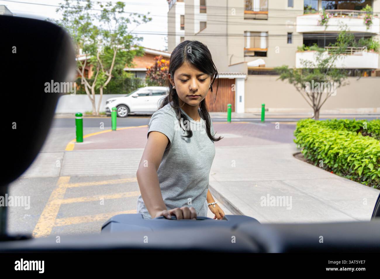 Un adolescent monte dans une voiture. La voiture est garée sur le bord de la route. La femme porte une chemise grise Banque D'Images Un adolescent monte dans une voiture. La voiture est garée sur le bord de la route. La femme porte une chemise grise Banque D'Images