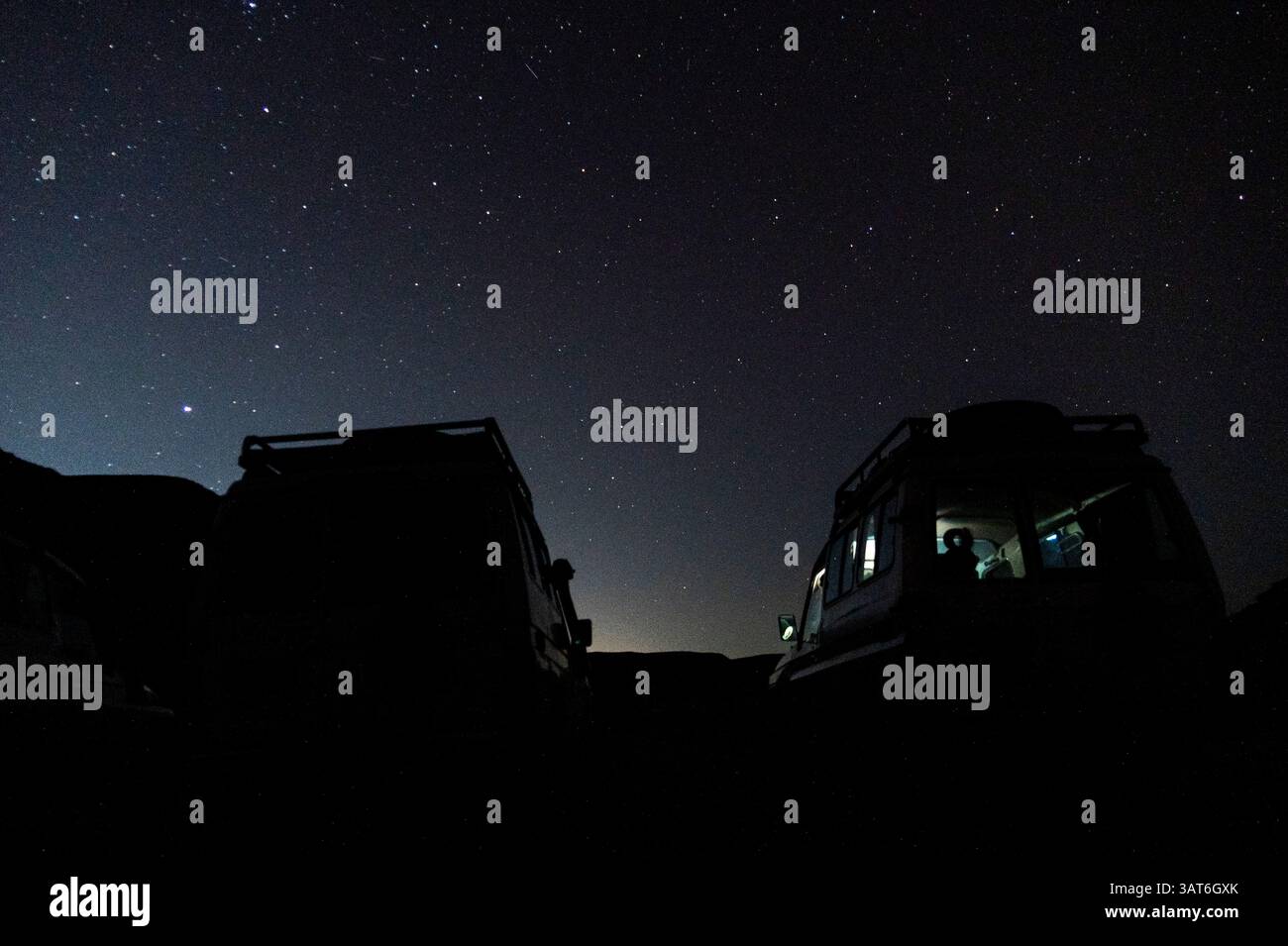 Silhouettes de deux véhicules contre un ciel étoilé nocturne, avec une faible lueur à l'horizon. Banque D'Images