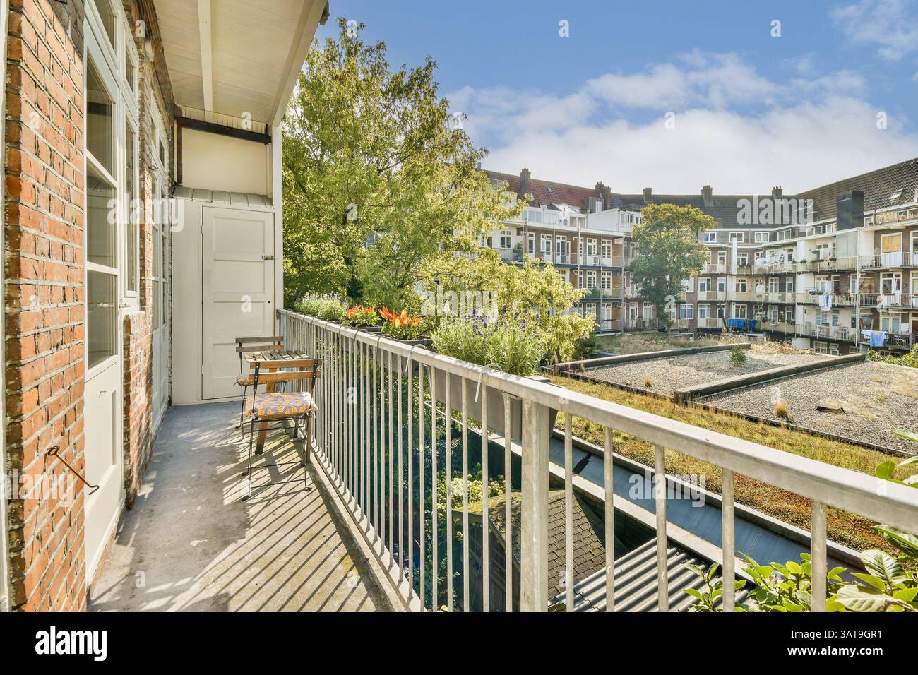 Un balcon serein avec vue sur la verdure luxuriante et des sièges confortables, encadrés par des bâtiments charmants dans une cour urbaine paisible par une journée ensoleillée. Banque D'Images