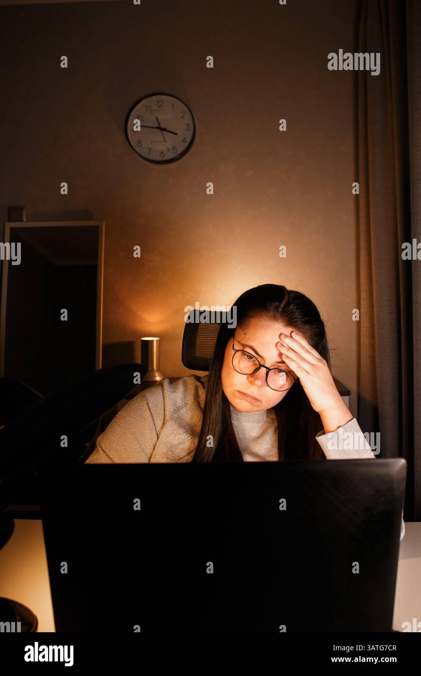 Femme travaillant sur l'ordinateur tard le soir au bureau à domicile. Concentrée femme freelance essayant de résoudre des problèmes d'affaires. Travailler et souffrir de nous Banque D'Images