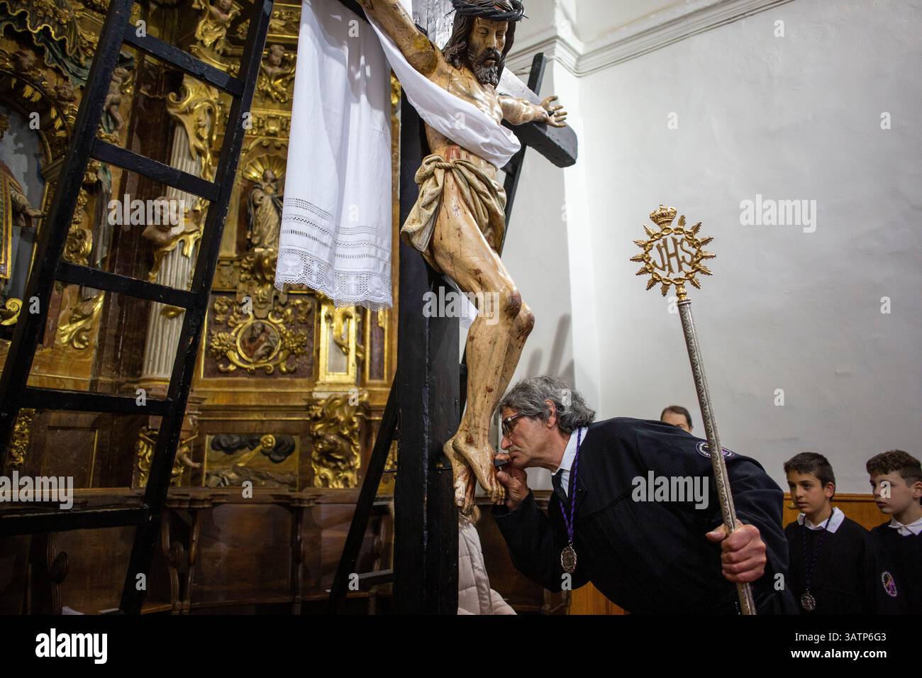 Sahagun, Espagne. 18 avril 2025. Membre de la fraternité de notre Père Jésus de Nazareth et patronage de Saint Joseph, touche avec respect les pieds de l'image articulée du Christ crucifié, lors de la messe à l'église de San Lorenzo et de la procession funéraire Sainte dans les rues de Sahagun. (Photo de Luis Soto/SOPA images/SIPA USA) crédit : SIPA USA/Alamy Live News Banque D'Images