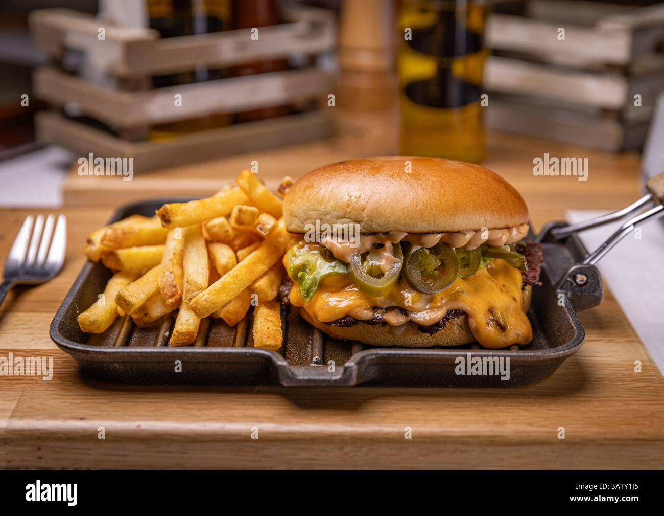 Délicieux cheeseburger avec frites, jalapenos et sauce servis sur une plaque chauffante Banque D'Images