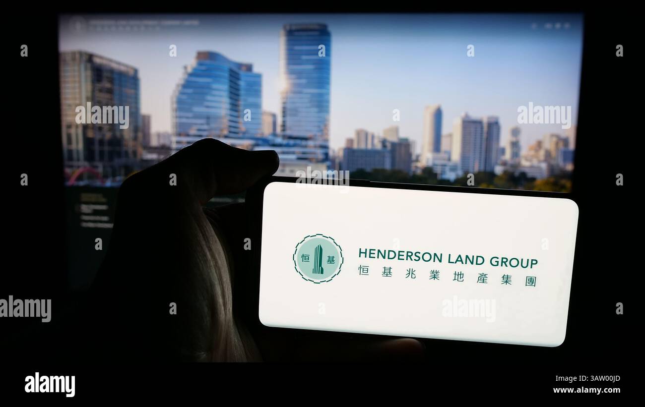 Dans cette illustration photo, une personne tient un téléphone portable avec le logo de la société Henderson Land Development Co. Ltd sur l'écran devant la page Web. Banque D'Images Dans cette illustration photo, une personne tient un téléphone portable avec le logo de la société Henderson Land Development Co. Ltd sur l'écran devant la page Web. Banque D'Images