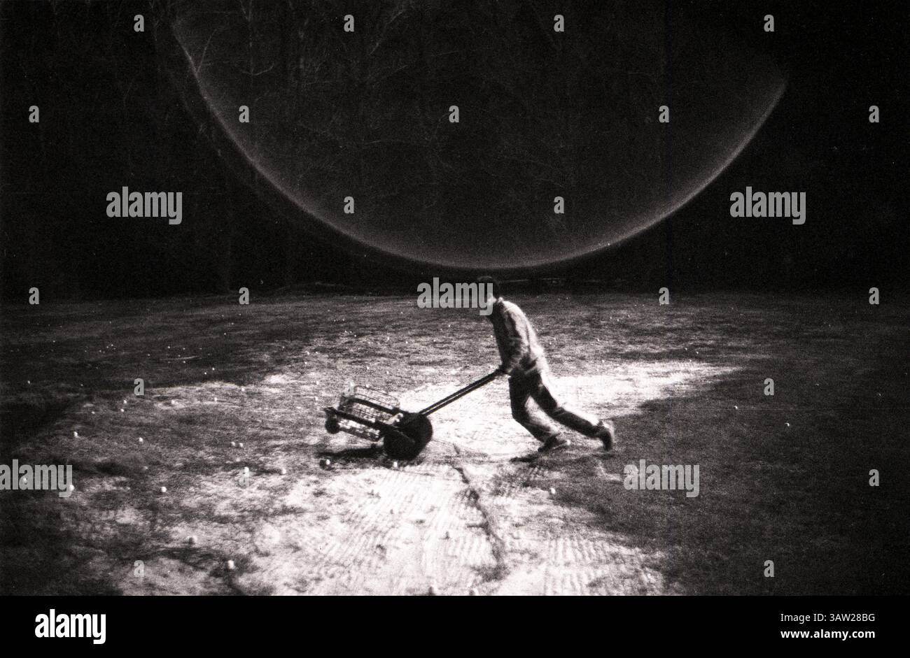 Luttant contre les ombres, un personnage déterminé pousse une charrette sous un dôme céleste étrange au crépuscule : Golf Caddie collectant des balles sous un éclairage dramatique Halo Banque D'Images