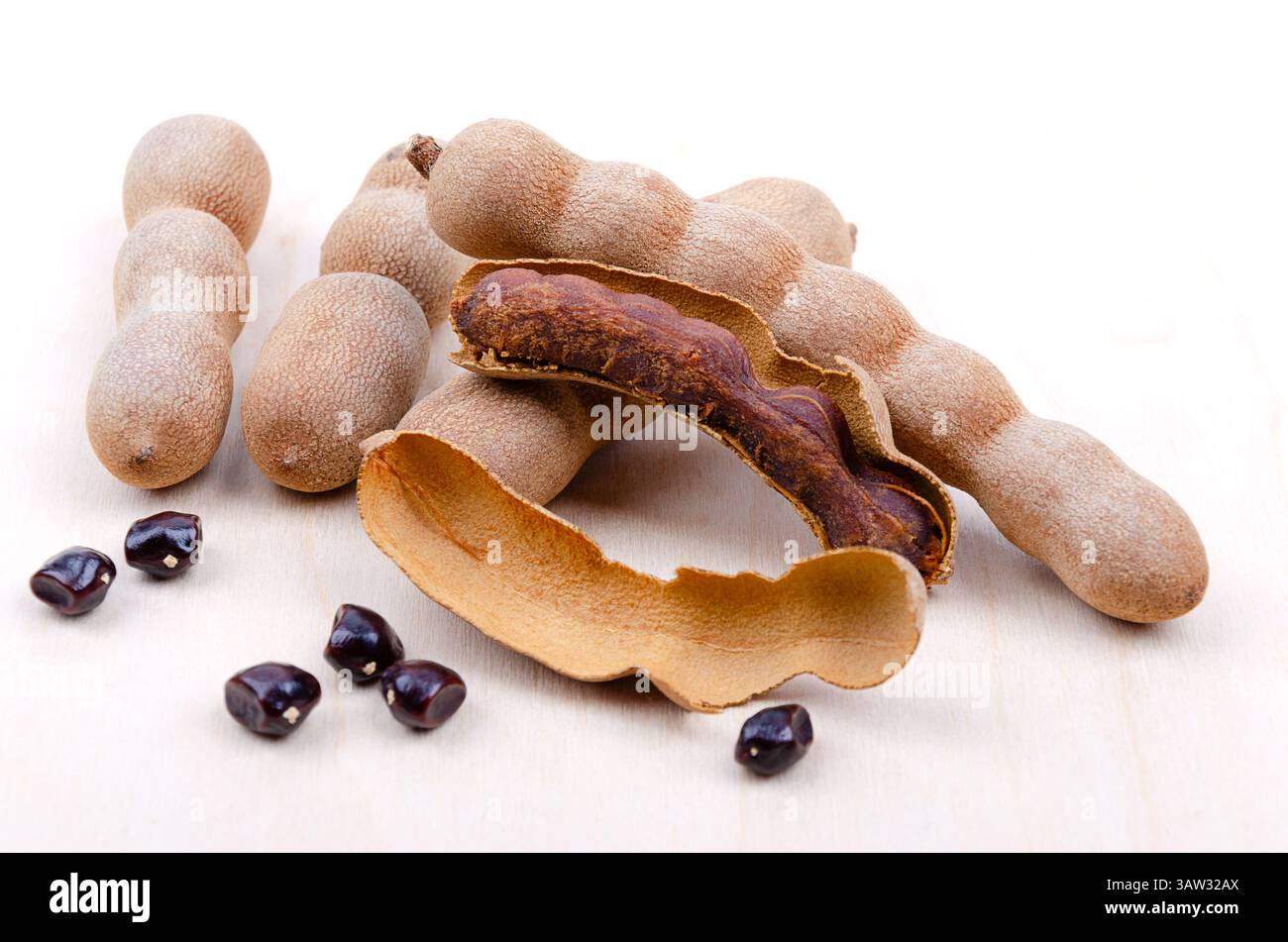 Fruits de tamarin, entiers, fendus, et graines, sur une surface en bois. Fruits bruns en forme de gousses de Tamarindus indica, avec une saveur aigre-douce. Banque D'Images