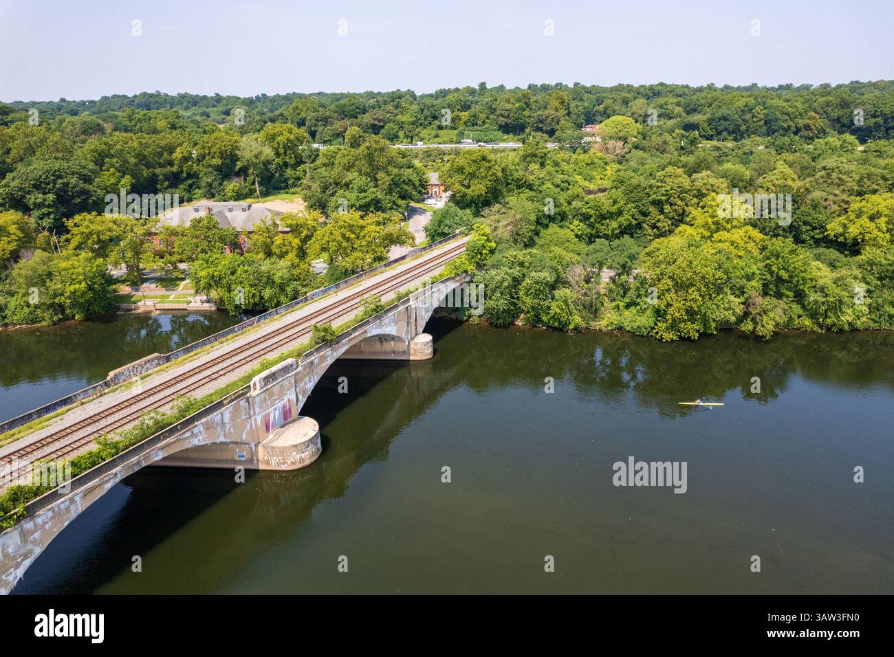 Un pont sur la rivière Schuykill avec un train sur les rails. Le pont est vieux et porte des graffitis dessus. L'eau est calme et les arbres sont luxuriants et g Banque D'Images Un pont sur la rivière Schuykill avec un train sur les rails. Le pont est vieux et porte des graffitis dessus. L'eau est calme et les arbres sont luxuriants et g Banque D'Images