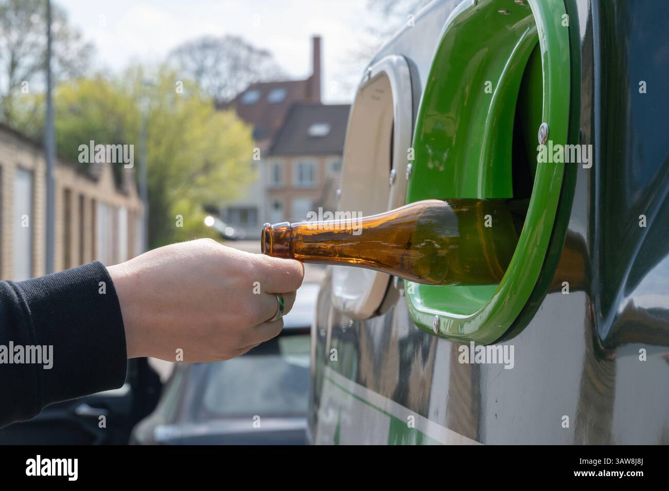 Une personne dépose une bouteille en verre dans un bac de recyclage, favorisant ainsi les efforts de durabilité dans la communauté Banque D'Images