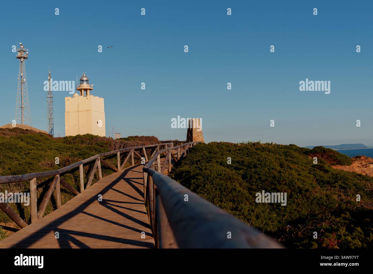 Vue panoramique sur une passerelle en bois menant à un phare sur un promontoire, surplombant la côte et la mer au coucher du soleil Banque D'Images